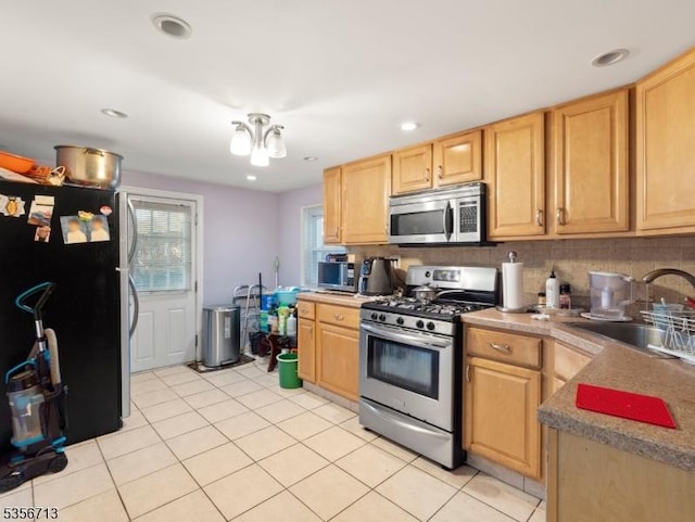 kitchen with stainless steel appliances, a sink, light tile patterned floors, light brown cabinetry, and decorative backsplash