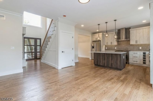 kitchen with wall chimney exhaust hood, appliances with stainless steel finishes, a center island, ornamental molding, and tasteful backsplash