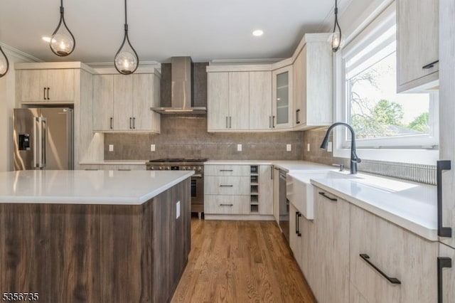 kitchen featuring stainless steel appliances, wall chimney range hood, light brown cabinetry, a sink, and light countertops