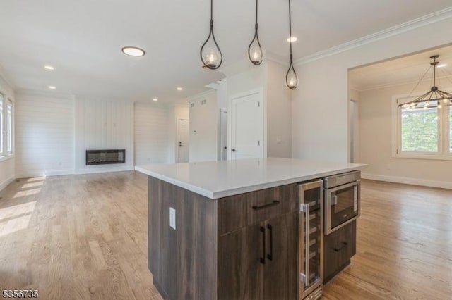 kitchen with baseboards, light wood-style flooring, crown molding, a center island, and a large fireplace