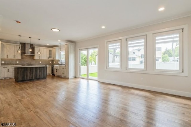 kitchen featuring wall chimney range hood, ornamental molding, a kitchen island, backsplash, and light countertops