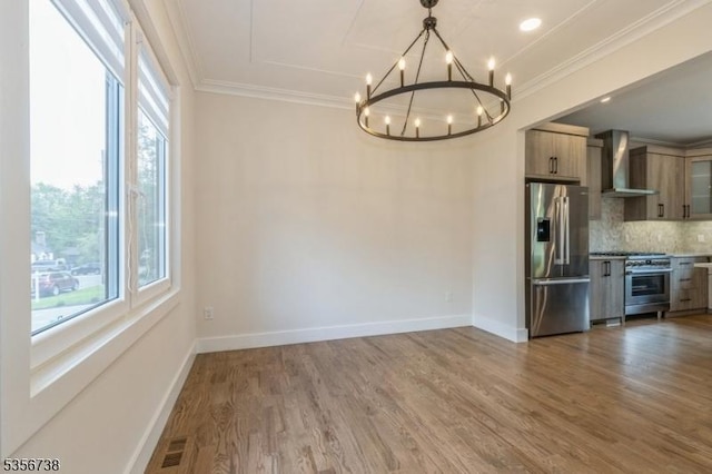 unfurnished dining area with a chandelier, ornamental molding, wood finished floors, and baseboards