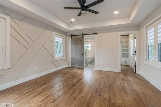 unfurnished bedroom with a barn door, multiple windows, wood finished floors, and a decorative wall