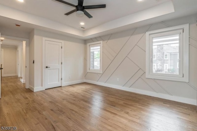 unfurnished bedroom with baseboards, wood finished floors, a raised ceiling, recessed lighting, and a ceiling fan