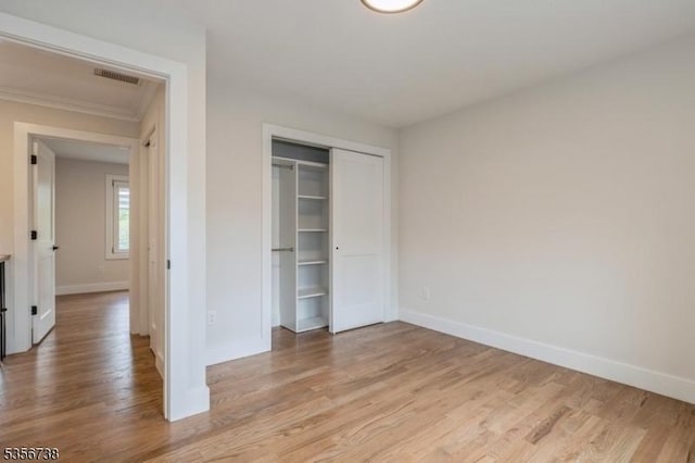 unfurnished bedroom with baseboards, light wood-type flooring, a closet, and ornamental molding