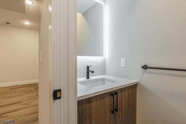 bathroom featuring vanity, wood finished floors, baseboards, and recessed lighting