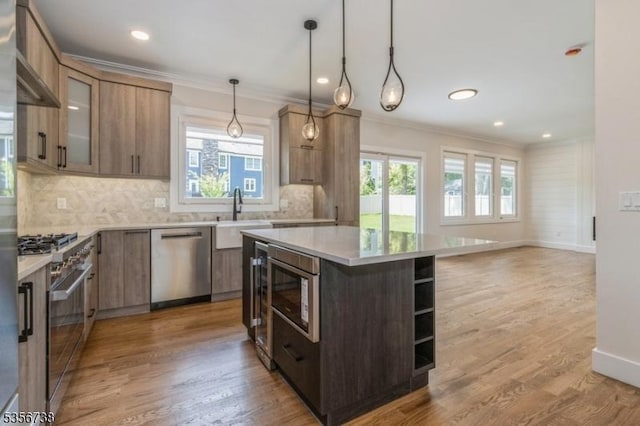 kitchen with appliances with stainless steel finishes, a sink, ornamental molding, light countertops, and tasteful backsplash
