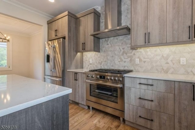 kitchen featuring stainless steel appliances, wall chimney range hood, crown molding, decorative backsplash, and light wood-style flooring
