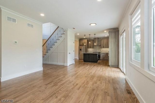 unfurnished living room featuring ornamental molding, healthy amount of natural light, light wood-style flooring, stairway, and baseboards