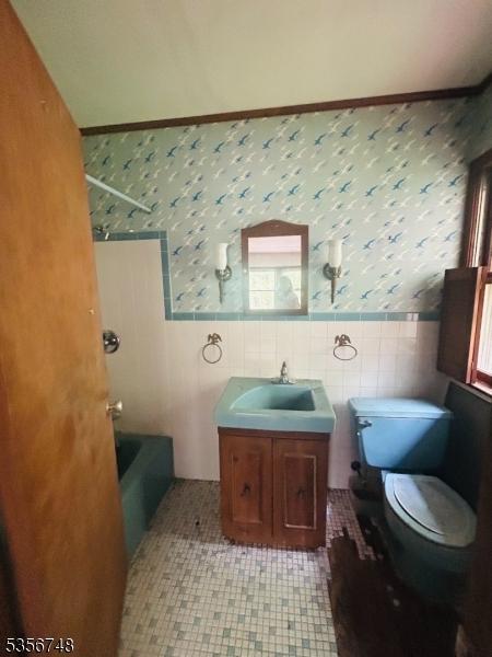 bathroom with wallpapered walls, a wainscoted wall, tile walls, vanity, and toilet