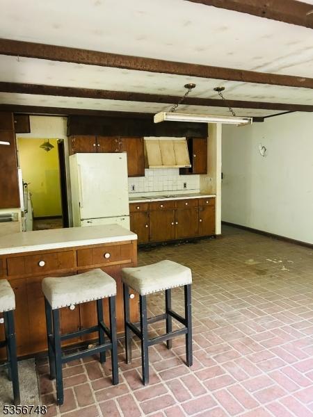 kitchen featuring freestanding refrigerator, brick patterned flooring, baseboards, light countertops, and backsplash