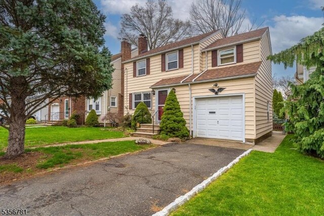view of front of home with a chimney, an attached garage, a front yard, and driveway