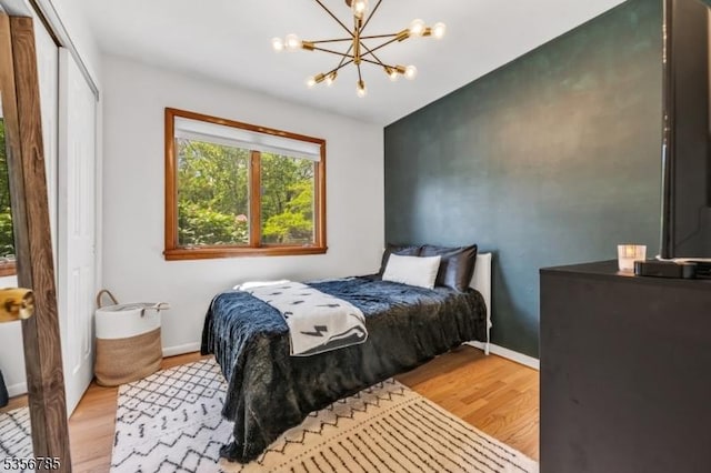 bedroom with wood finished floors, a chandelier, baseboards, and a closet