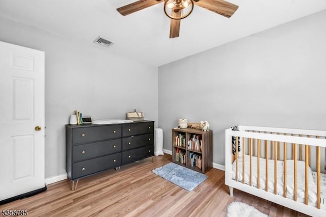 bedroom with light wood-style floors, a nursery area, ceiling fan, and baseboards