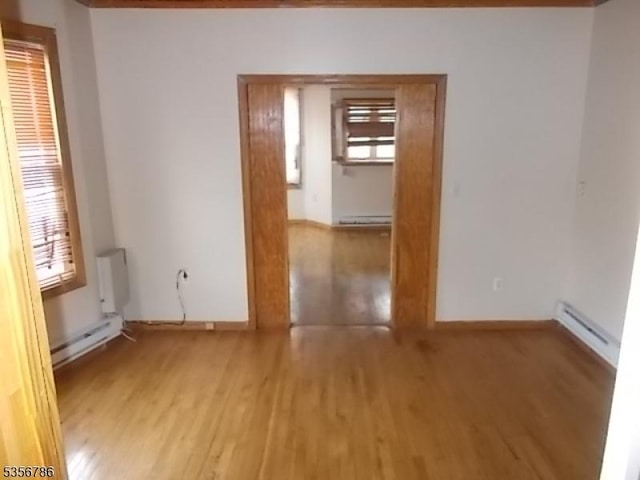 unfurnished room featuring a baseboard radiator, light wood finished floors, baseboards, and baseboard heating