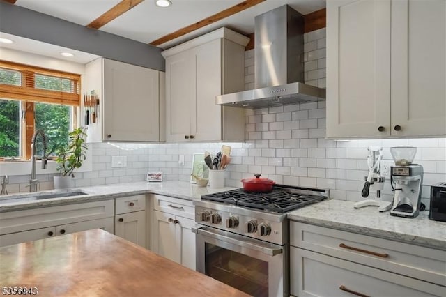 kitchen with wall chimney exhaust hood, high end stainless steel range oven, a sink, decorative backsplash, and recessed lighting