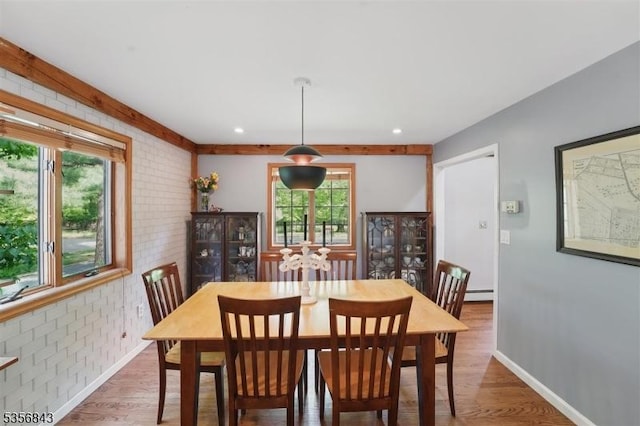 dining room with brick wall, wood finished floors, a baseboard heating unit, and baseboards
