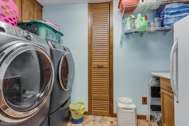 clothes washing area with washer and clothes dryer, cabinet space, and baseboards