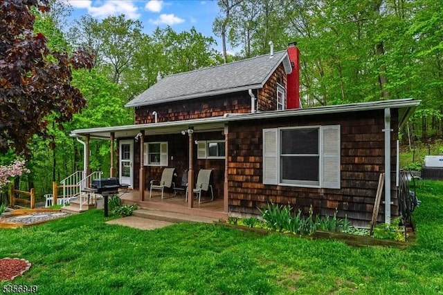 back of property with a chimney, a lawn, roof with shingles, and a porch
