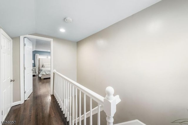 corridor with an upstairs landing, wood finished floors, vaulted ceiling, and baseboards