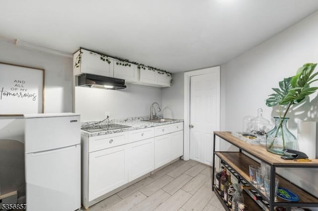 kitchen featuring freestanding refrigerator, a sink, black electric cooktop, white cabinetry, and under cabinet range hood
