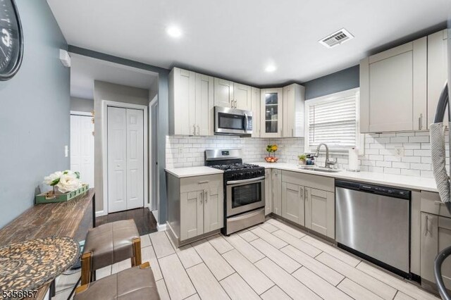kitchen featuring stainless steel appliances, a sink, gray cabinets, light countertops, and backsplash