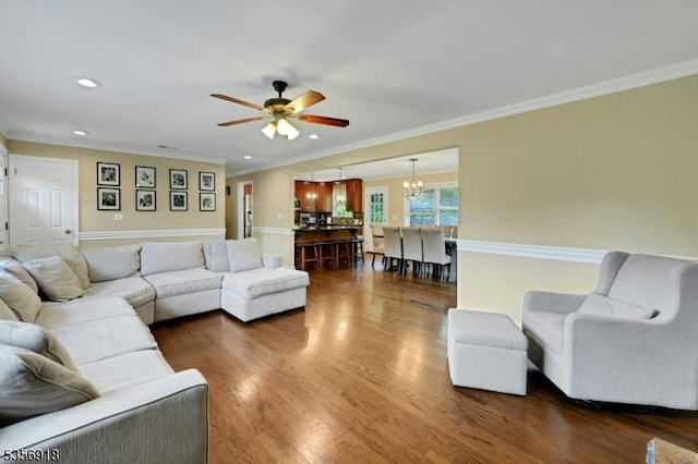 living room with a ceiling fan, a chandelier, ornamental molding, dark wood-style flooring, and recessed lighting