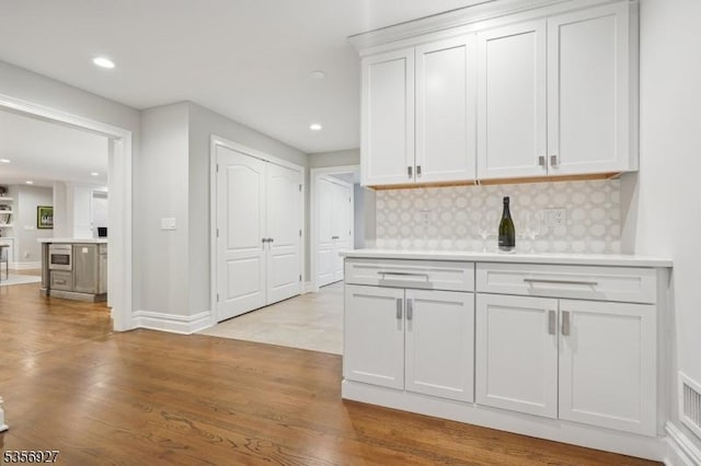 kitchen featuring tasteful backsplash, light countertops, white cabinetry, recessed lighting, and light wood-style floors