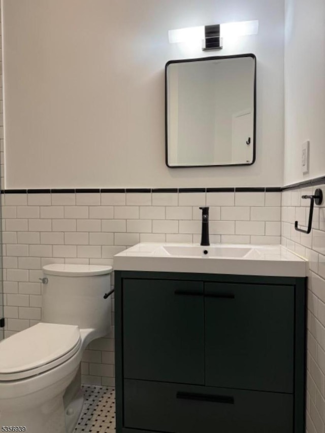 bathroom with tile walls, a wainscoted wall, vanity, and toilet
