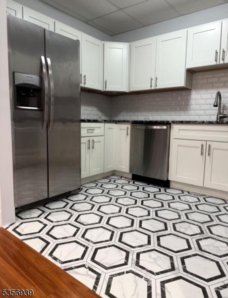 kitchen featuring appliances with stainless steel finishes, a drop ceiling, tasteful backsplash, and white cabinetry