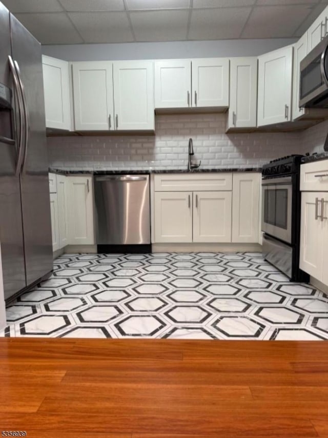 kitchen with stainless steel appliances, a drop ceiling, white cabinets, tasteful backsplash, and a sink