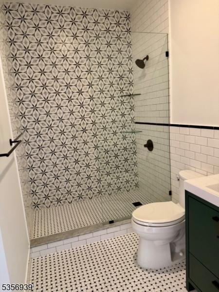 bathroom featuring toilet, a stall shower, tile walls, vanity, and tile patterned flooring