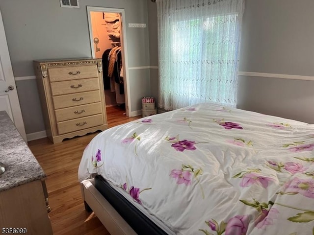 bedroom with a spacious closet, wood finished floors, a closet, and baseboards