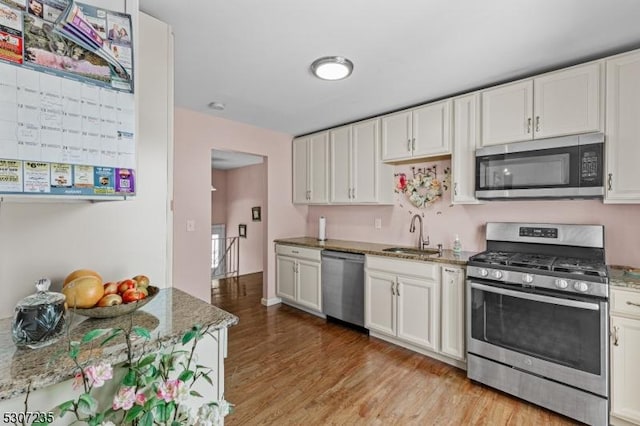 kitchen with stainless steel appliances, a sink, light wood-type flooring, and white cabinets