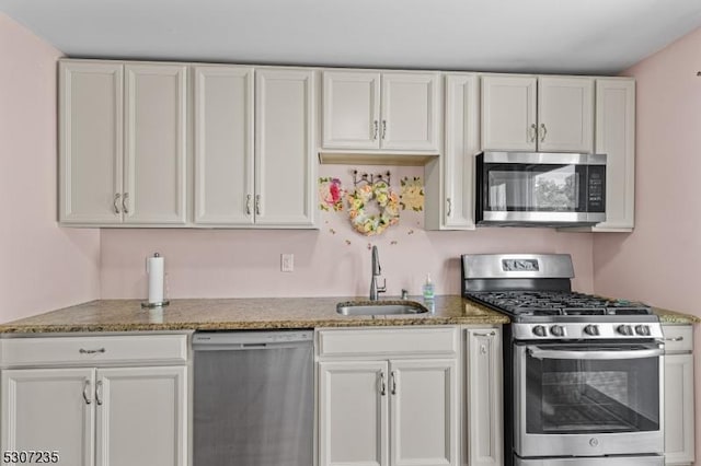 kitchen featuring appliances with stainless steel finishes, a sink, white cabinetry, and light stone counters