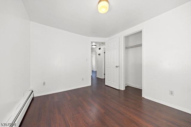 unfurnished bedroom featuring a baseboard heating unit, wood finished floors, baseboards, and a closet