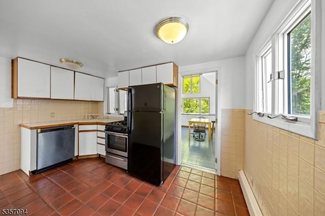 kitchen featuring appliances with stainless steel finishes, tile walls, white cabinets, dark tile patterned flooring, and a baseboard heating unit