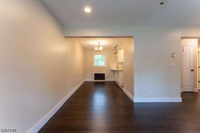 hall featuring dark wood-type flooring, baseboards, and a chandelier