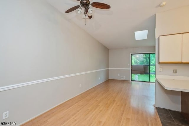 unfurnished living room featuring a skylight, lofted ceiling, wood finished floors, and a ceiling fan