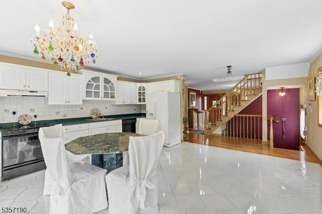 kitchen featuring black appliances, dark countertops, under cabinet range hood, a chandelier, and glass insert cabinets
