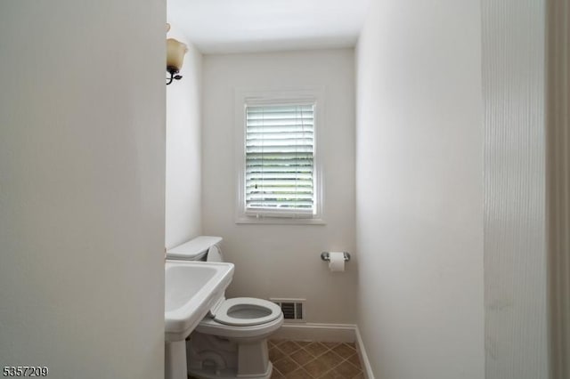 half bath with toilet, baseboards, and tile patterned floors