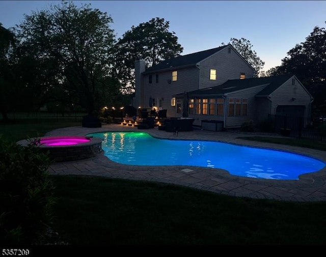 pool at dusk with a patio, a pool with connected hot tub, a sunroom, and fence