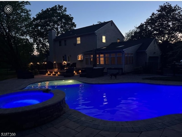 pool at dusk with a pool with connected hot tub, a patio area, a sunroom, and an outdoor living space with a fire pit
