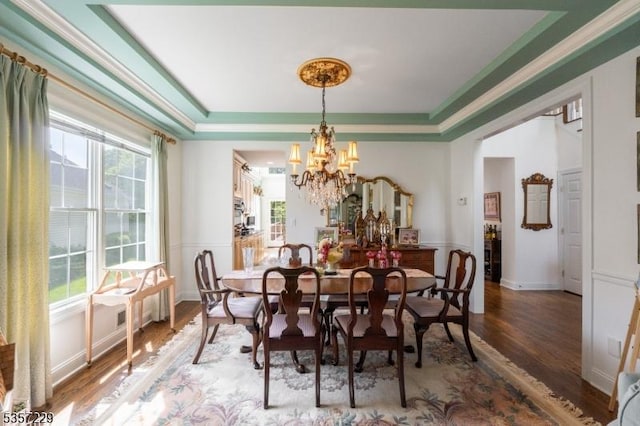 dining space featuring wood finished floors, a chandelier, healthy amount of natural light, and a tray ceiling