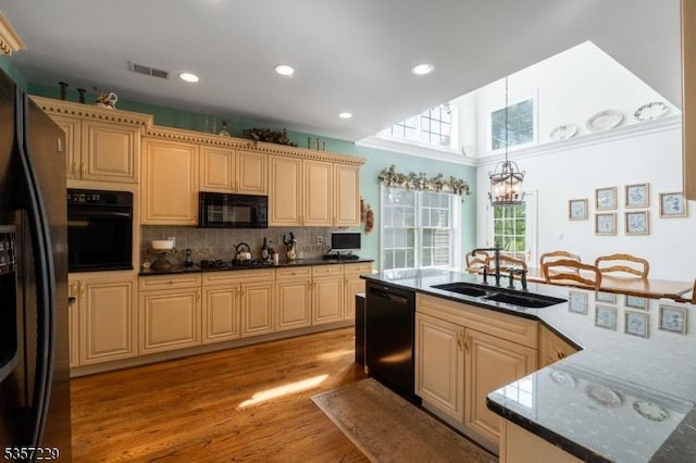 kitchen with black appliances, a sink, a chandelier, light wood-style flooring, and decorative backsplash