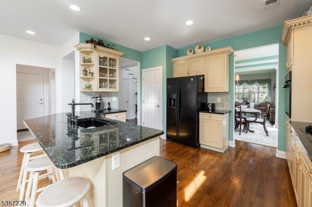 kitchen featuring black appliances, a sink, cream cabinetry, a breakfast bar area, and dark wood-style flooring