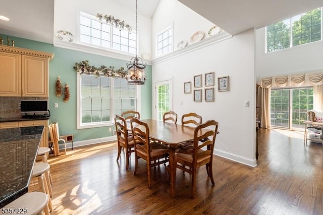 dining space with a high ceiling, a chandelier, baseboards, and wood finished floors