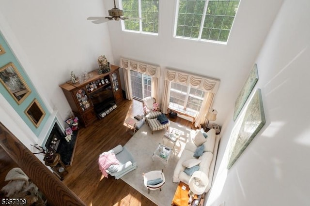 living area featuring a high ceiling, wood finished floors, plenty of natural light, a ceiling fan, and a fireplace