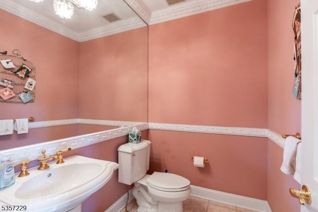half bathroom featuring a sink, toilet, tile patterned flooring, baseboards, and crown molding