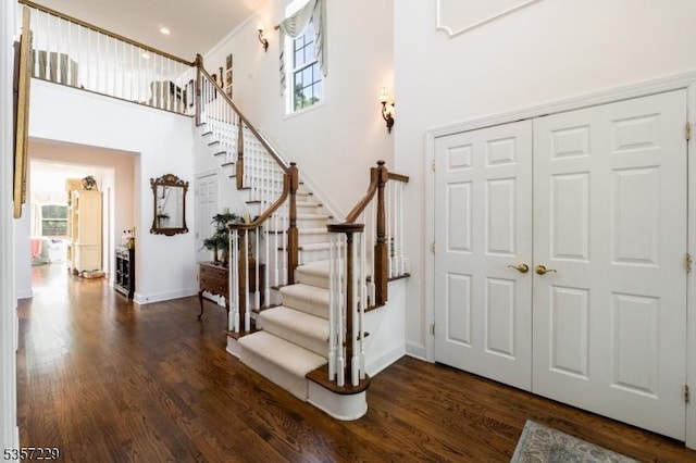 foyer entrance with healthy amount of natural light, dark wood-style floors, stairs, baseboards, and a towering ceiling